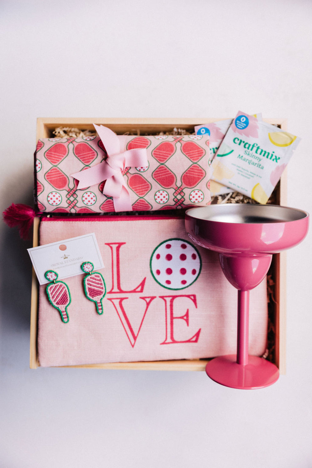 Curated Dink and Drink gift box tied with pink ribbon, featuring pickleball towel, earrings, LOVE bag, and margarita mix