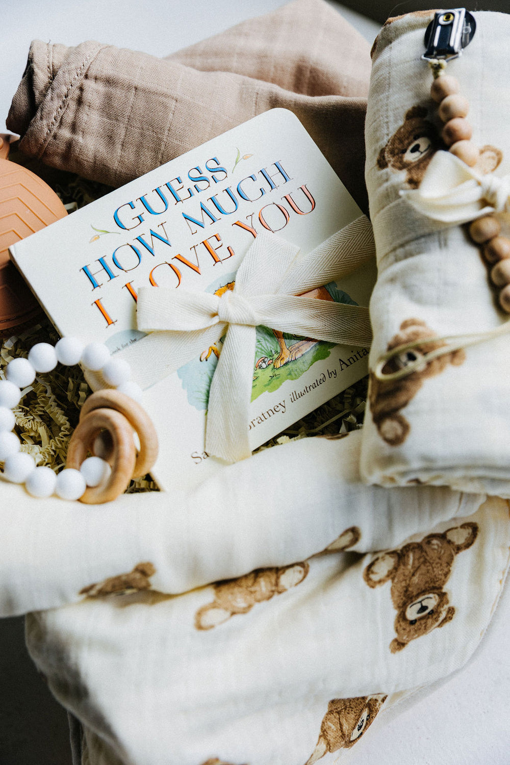 Children's book titled 'Guess How Much I Love You' with a organic cotton muslin swaddle and burp cloths as part of Welcome Little Bear gift box