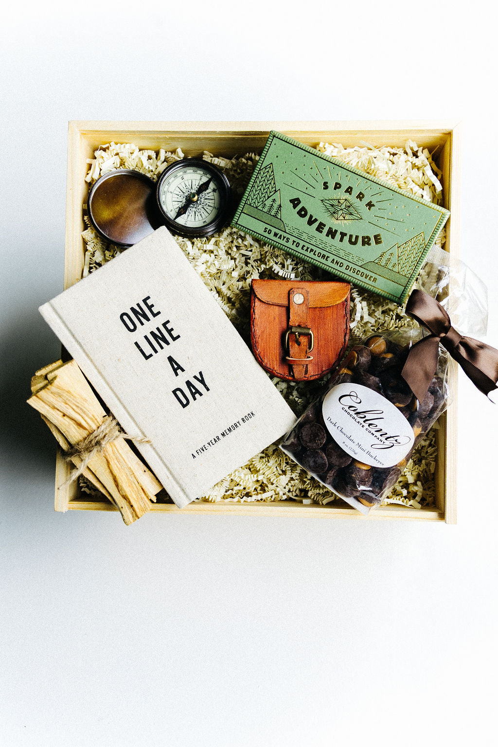 Adventure Awaits Gift Box with journal, leather compass case, Spark Adventure box, Palo Santo sticks, and dark chocolate buckeyes displayed in wooden keepsake box
