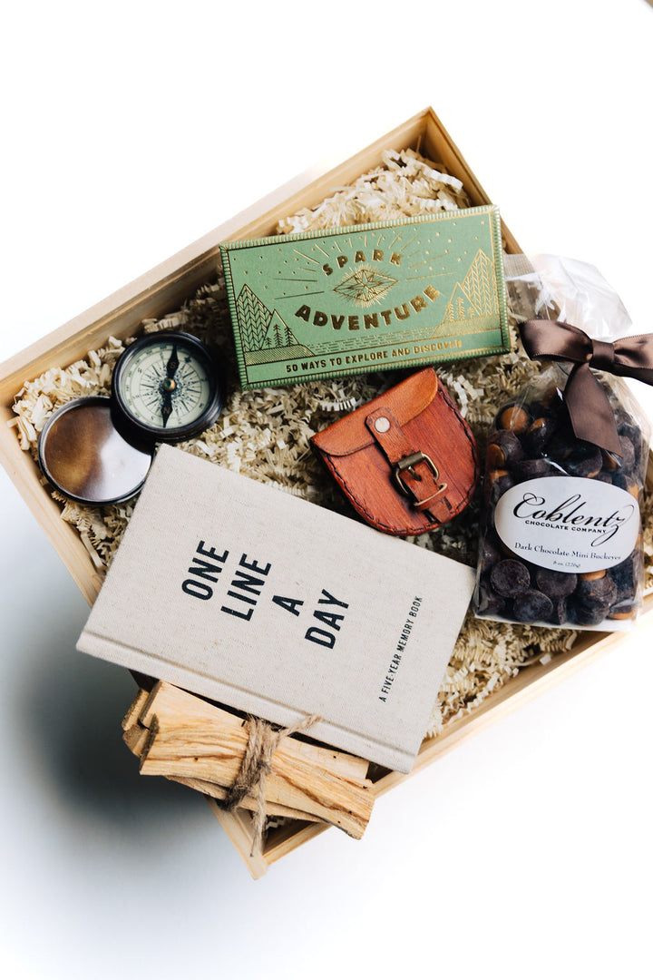 Top view of curated Adventure Awaits gift set with compass, chocolate buckeyes, Spark Adventure prompts, and journal