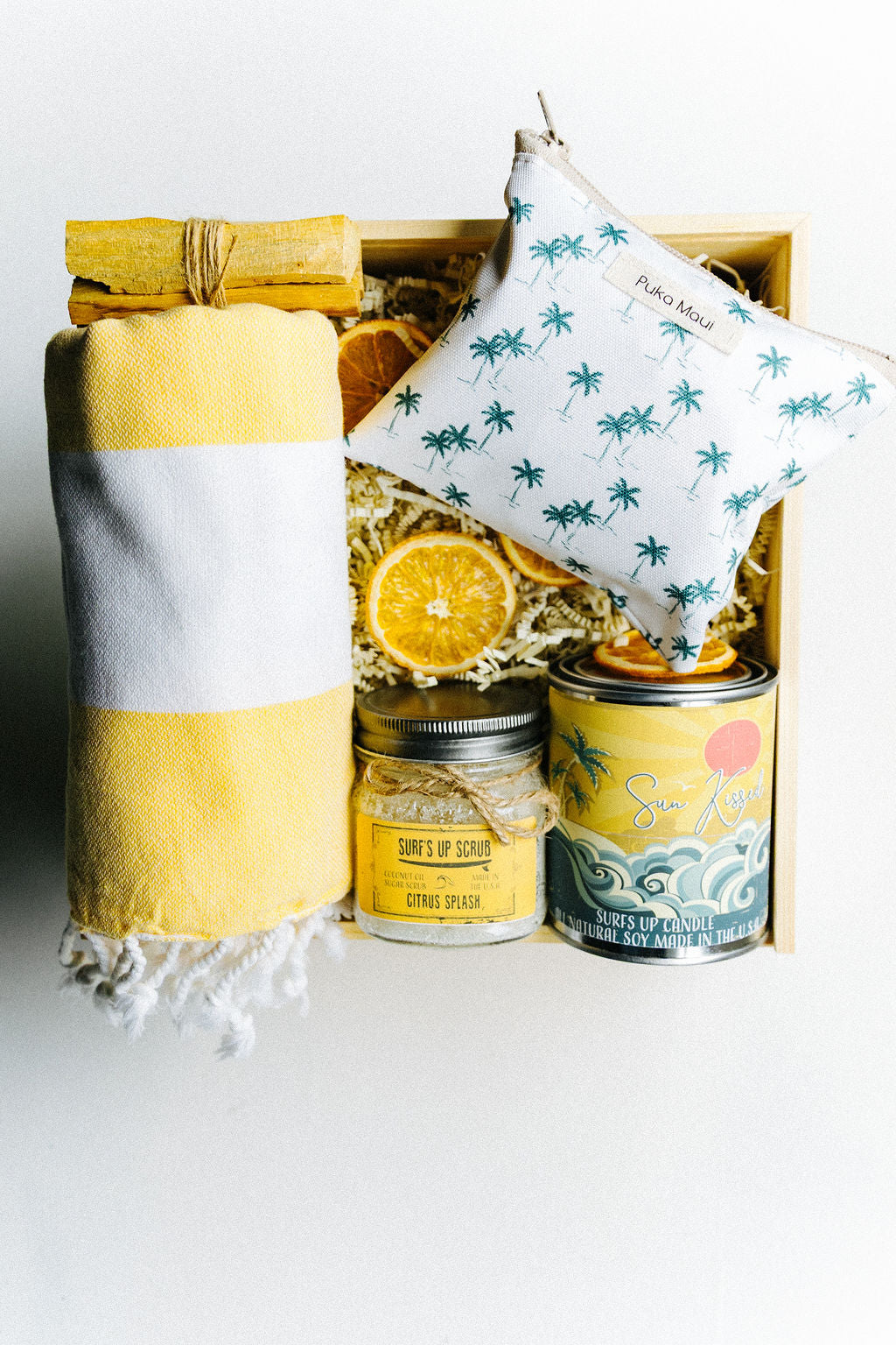 Top down view of Jupiter Beach Box contents including towel, white zippered pouch, candle, sugar scrub, and palo santo sticks