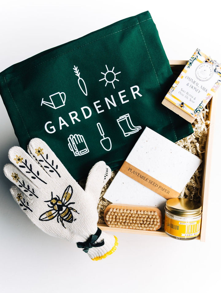 Wooden gift box filled with apron, bee gloves, soap, nail brush, seed paper, and tallow body butter on crinkle paper filler