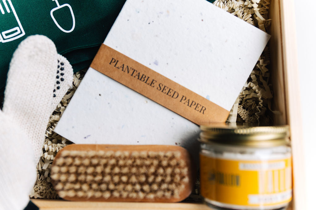 Plantable seed paper notebook next to nail brush and tallow body butter inside gift box