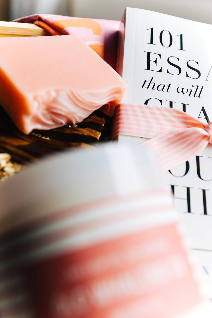 Close up of Pink magnolia artisan soap with bamboo soap dish beside the book 101 Essays That Will Change the Way You Think from Sunshine in a Bag gift set
