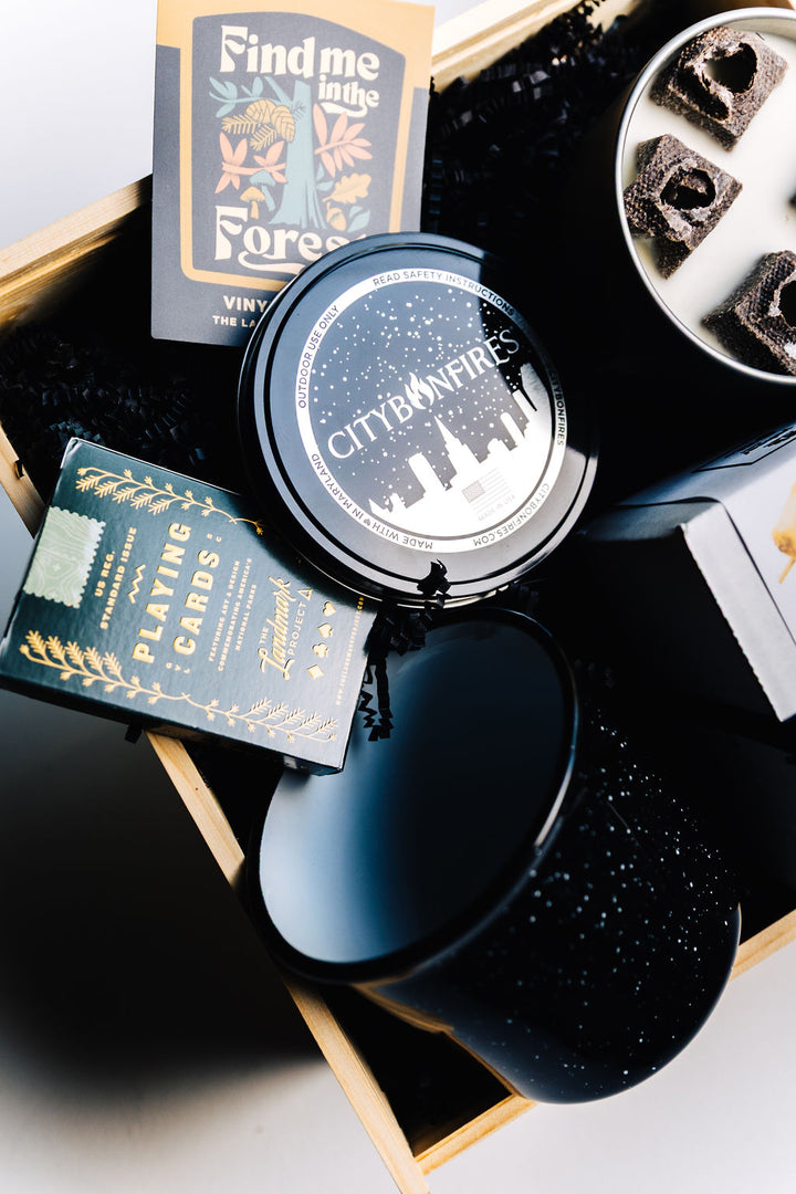 Portable fire pit, s’mores kit, and cozy mug in wooden box, styled with black crinkle filler