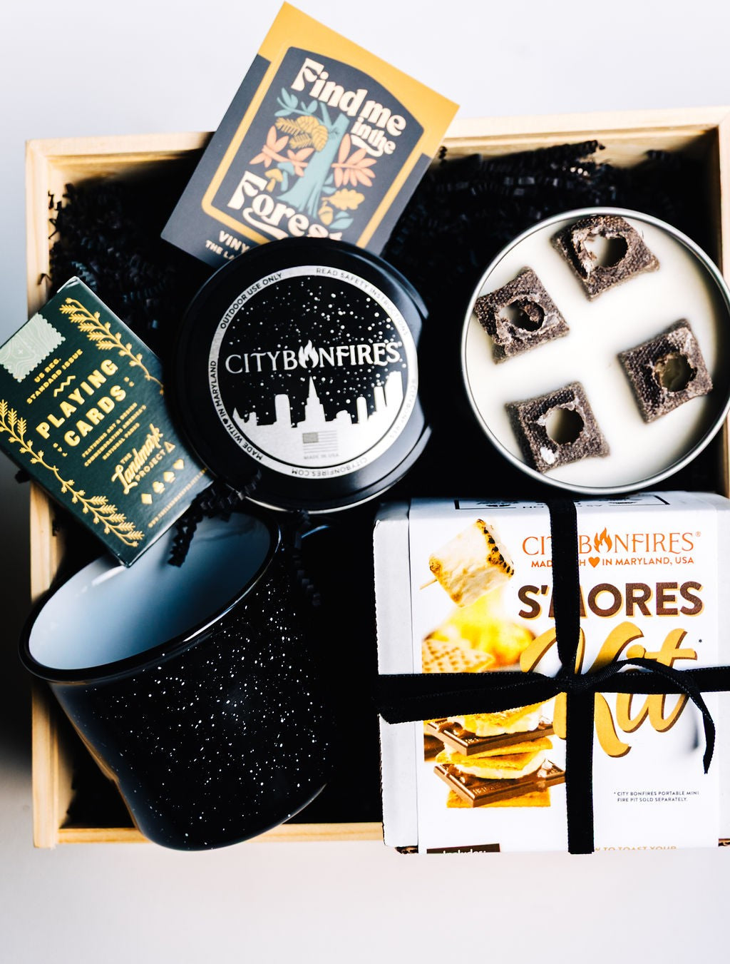 Wooden gift box styled with s’mores kit, mug, candle, playing cards, and sticker for rustic presentation