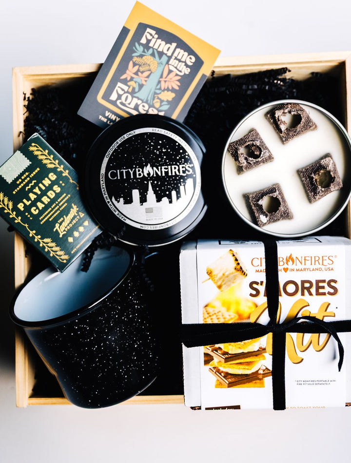 Wooden gift box styled with s’mores kit, mug, candle, playing cards, and sticker for rustic presentation