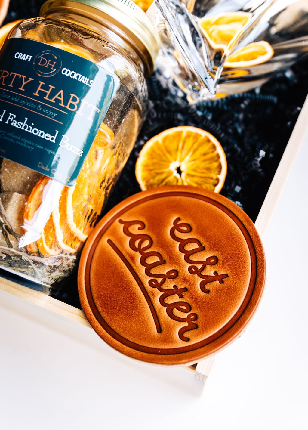 Close-up of East Coaster leather coaster and cocktail mix jar with dried orange garnish for Old Fashioned drink
