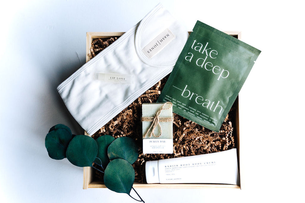 Top view of Pure & Simple natural skincare gift box with sheet mask, bamboo headband, soap, and body crème in wooden box with filler.