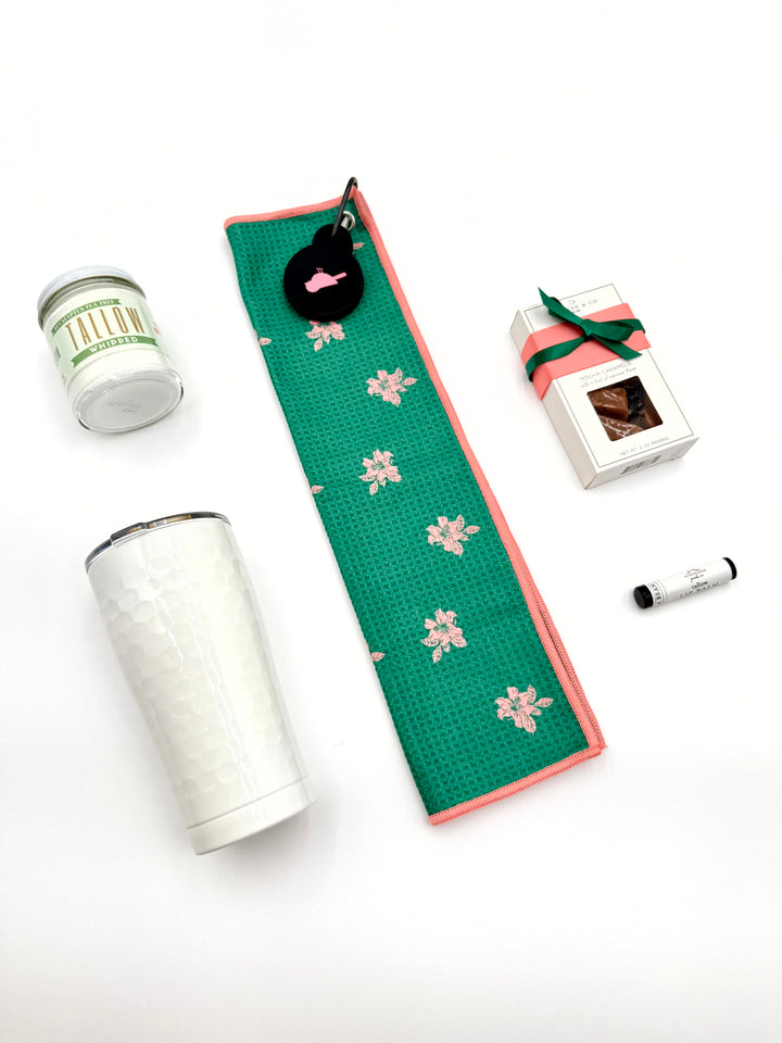 Fore Her golf gift box contents displayed flat – tumbler, towel, tallow moisturizer, lip balm, and caramels