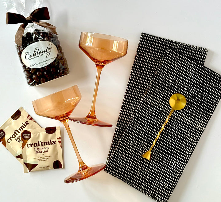 Flat lay of espresso martini cocktail kit, amber crystal glasses, and cotton napkins
