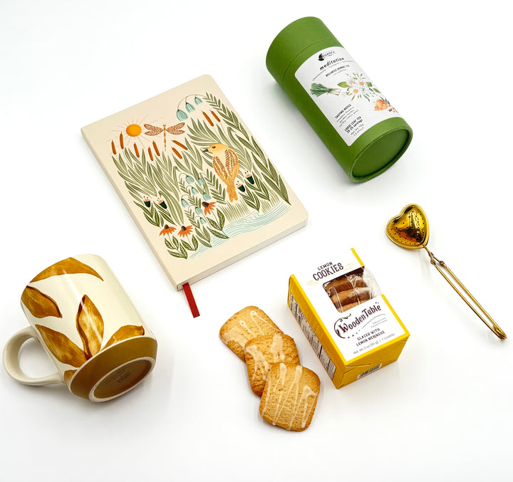 Flat lay of Steeped in Stillness Gift Box contents – journal, tea canister, cookies, mug, and heart-shaped infuser
