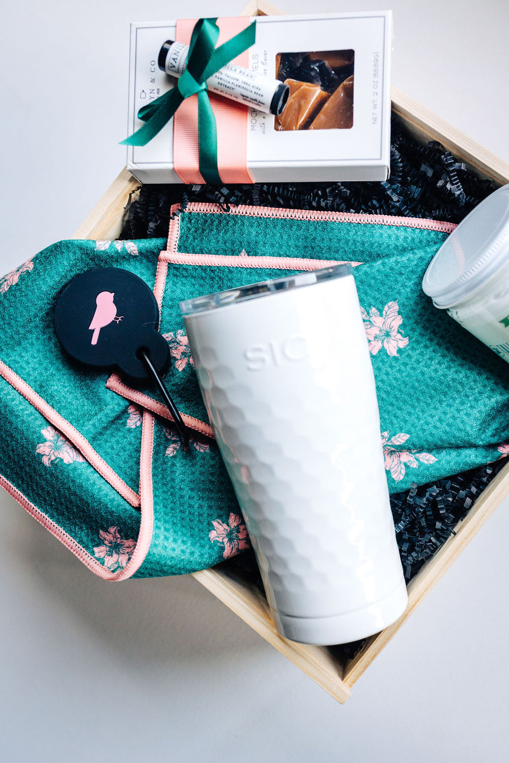 Close-up of Fore Her golf gift set featuring tumbler, Augusta floral towel, and mocha caramels tied with pink and green ribbon.