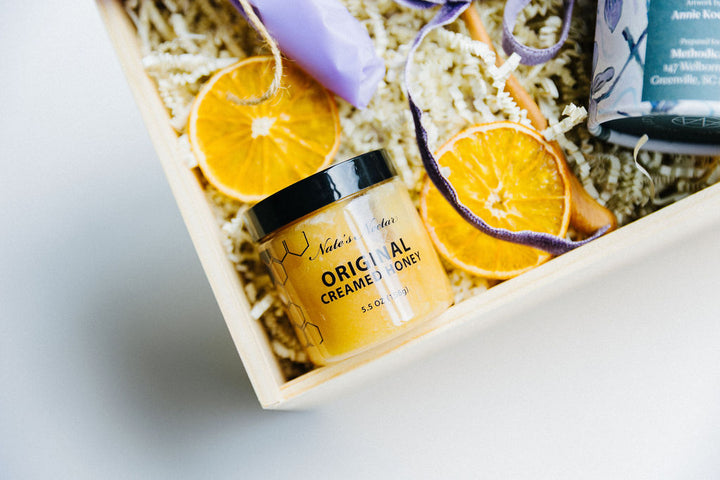 Close-up of Nate’s Nectar creamed honey jar nestled in luxury gift box with dried citrus and wooden spoon.