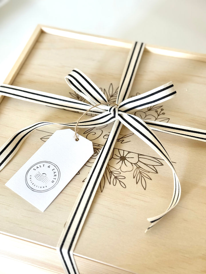 Luxury wooden gift box lid with floral custom engraving design, tied with striped ribbon and Salt & Earth gift tag.